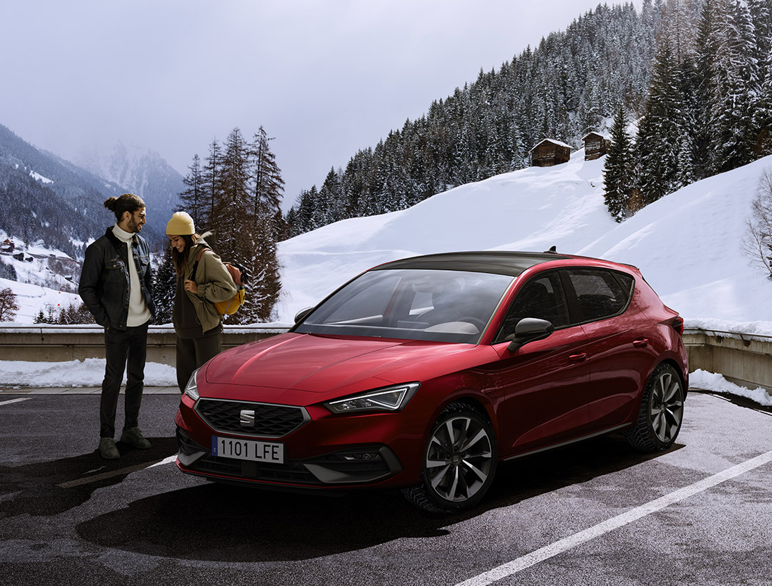 Ein Paar unterhält sich neben einem SEAT Leon in Desire Red in einer verschneiten Berglandschaft