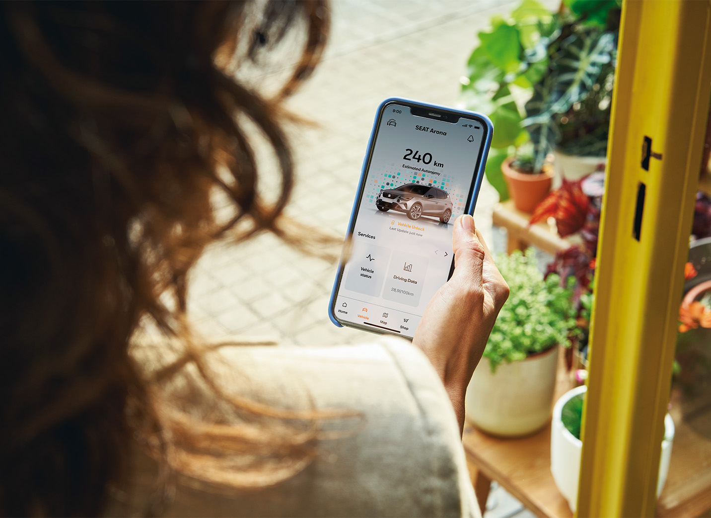 Donna che utilizza un’app mobile per connettersi alla sua SEAT Arona e scaricare gli aggiornamenti OTA, piante sullo sfondo